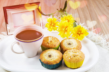 Cup hot cocoa or hot chocolate and banana cupcake in white plate on table with yellow fake flowers with bokeh heart light background, Concept time of rest enjoy in winter.