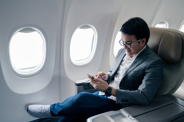Young asian businessman with suit sitting in business first class seat via using smartphone with...