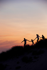 Obraz premium Sylwetka rodziny biegnącej przez wydmy