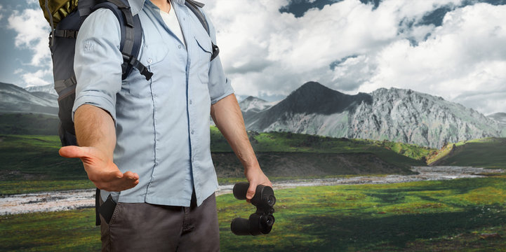 Uunrecognizable Young Traveler Man With A Baclpack And Binoculars, Stretches Out His Hand Mountains. Help In Travel Concept