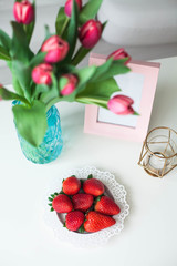 Interior. Coffee table, sofa, candle. A bouquet of tulips in a glass vase, strawberry. A room for rest. Bright hues. Spring. Cozy.