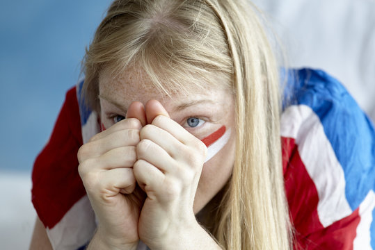 Sports enthusiast watching match with hands clasped anxiously to face