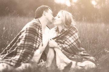 Happy couple - pregnant woman and her husband in the park covered with a warm blanket