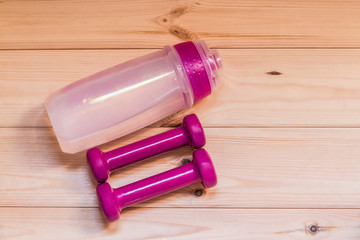 Two pink dumbells and water bottle on wooden background. Fitness and health.