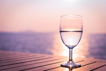 Silhouette glass of wine on a wooden table with  seascape and skyline in the evening with sunset tone style.