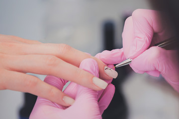 Closeup shot of manicurist in pink rubber gloves paints pattern with brush on female nails. Professional manicure and nail art in beauty salon