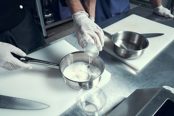 the chef prepares the dish in a frying pan. Hands close-up of chefs. Frying pan on the stove