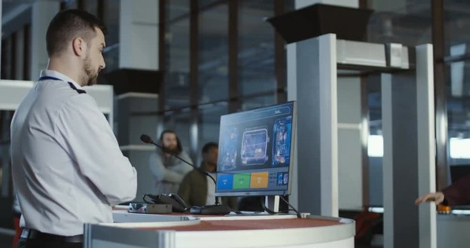 Man in uniform standing at counter at checking point and watching at monitor with x-ray of luggage. 4K shot on Red cinema camera.