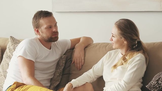 Happy couple man and woman sitting on cozy sofa and talking in room interior