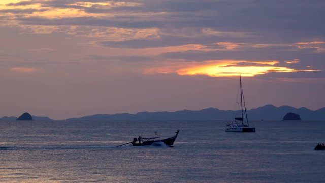 Catamaran in the roadstead and a long-tail boats floating in the sea at sunset