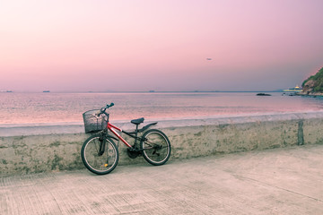 Obraz premium Lonely bicycle with basket standing on concrete pier. Seascape background at sunset golden hour. Toned image.