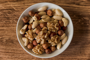 nuts, in a white bowl, fried on a dark wood background, mixture of walnuts, almonds and roasted nuts, top view