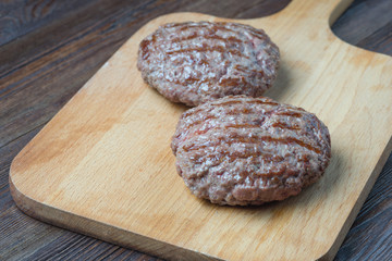 Two grilled hamburger patty on cutting board