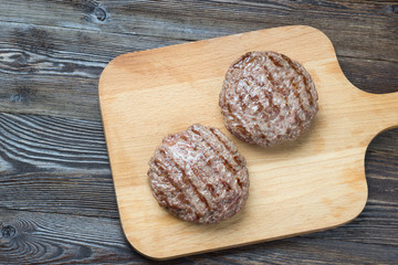 Two grilled hamburger patties on wooden background