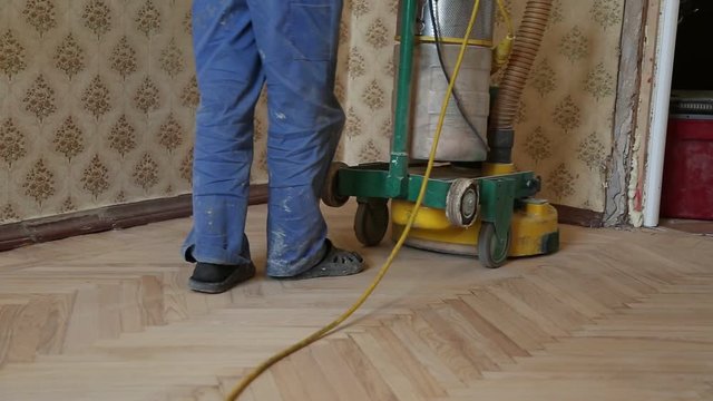Worker polishing old wooden parquet floor with grinding machine
