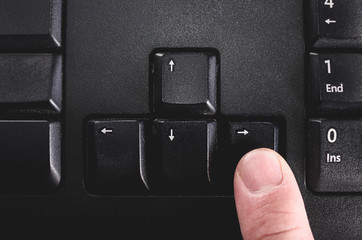 Human finger pressing the directional right key from a black keyboard