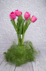 spring pink tulips in a glass vase with grass on grey background