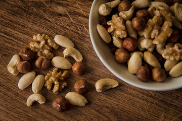 nuts, in a white bowl, fried on a dark wood background, mixture of walnuts, almonds and roasted nuts, top view