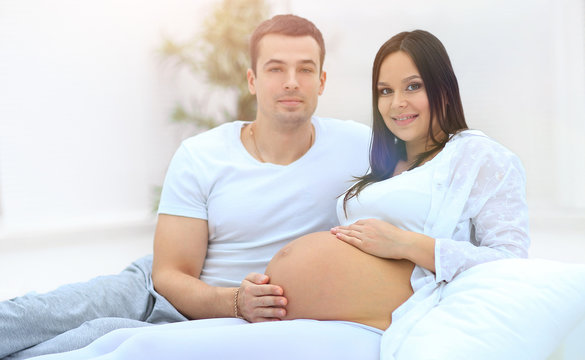 Happy pregnant woman and partner sitting on bed with hands touch