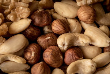 nuts, in a white bowl, fried on a dark wood background, mixture of walnuts, almonds and roasted nuts, top view