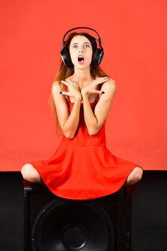 Girl with loose hair wears headphones and red dress.