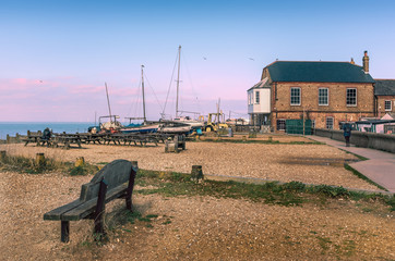 Whitstable, Kent, UK beach with wooden benches and old wooden boats moored on the beach. There is a...