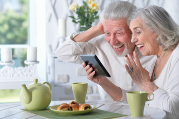 senior couple using tablet while drinking tea