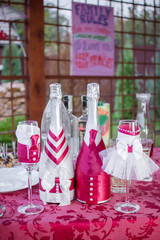 Decoration of the wedding table, glasses of the groom and the bride and two bottles of champagne decorated as the bride and groom. Closeup.
