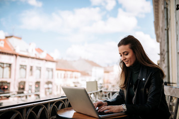 Woman working on a laptop while sitting on the terrace at the city. Freelance work concept.