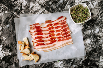 Smoked bacon slices, bread and herbs on baking paper. Preparation of tasty snack.