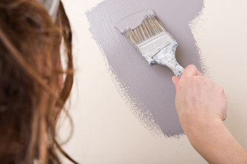 Young woman is painting wall with brush in bathroom under remodeling