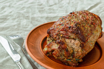 on a light linen rumpled tablecloth is a plate with a juicy baked meat roll and a number lie a knife for meat and a fork