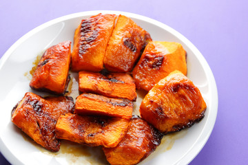 Pumpkin, ultraviolet background, baked pumpkin with honey, white plate with orange vegetables, pop art, slices of pumpkin on purple background, vegetarianism, healthy food, art