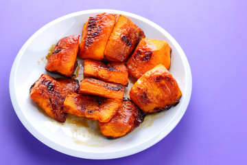 Pumpkin, ultraviolet background, baked pumpkin with honey, white plate with orange vegetables, pop art, slices of pumpkin on purple background, vegetarianism, healthy food, art