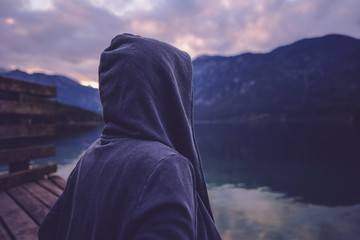 Lonely hooded female person standing by the lake Bohinj in Slovenia in sunset