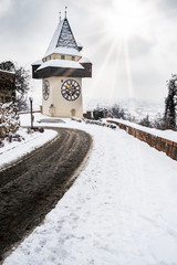 Sun flares over snow covered Uhrturm clocktower landmark of Graz