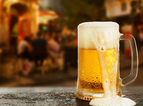 Mug with beer on the background of a outside bar.