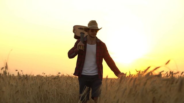young guy walks the golden wheat field in the rays of the sunset with guitar.
