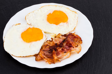 Breakfast with fried eggs and bacon on dark stone background
