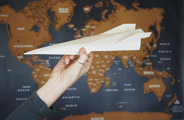 Mano sujetando un avión de papel con un mapamundi de fondo 