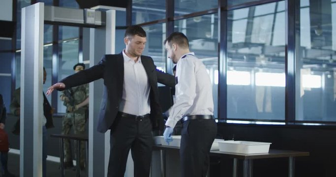 Airport Security Agent Using A Metal Detector On A Male Passenger In A Suit To Pat Him Down At The Boarding Gate After Passing Through The X-ray Scanner. 4K Shot On Red Cinema Camera.