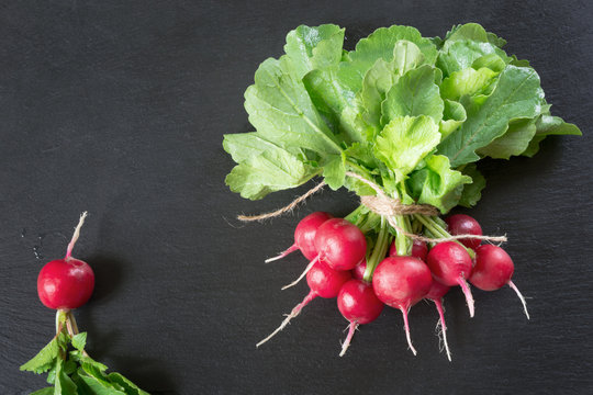 Red radish with foliage on black slate dish as background. Top view.