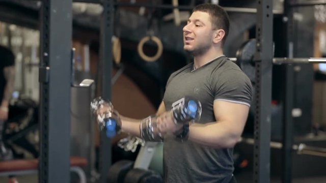 Strong man with an effort pumps his arm muscles with dumbbells. Brutal bodybuilder raises and releases heavy weight for building muscles in the gym.
