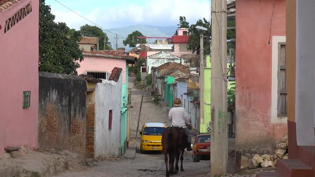 A beautiful shot of the buildings and cobblestone streets of Trinidad, Cuba with cowboy riding past.