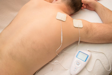 close-up of a doctor holding an electric muscle massager in the hand against a background of a blurred patient who has electrodes on his back