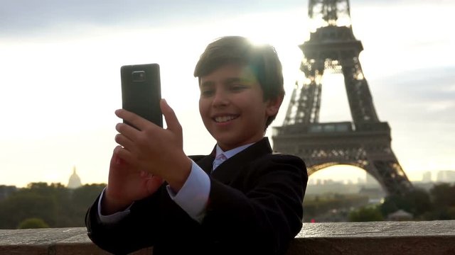 Boy in a suit taking selfie photo with his smartphone on the background of the Eiffel Tower