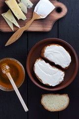 Hard cheese on a wooden board, sandwiches with soft cheese, honey in glass dishes, copy space, minimalism, cheese pattern, wooden dark background, healthy food, wooden cutlery
