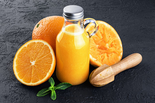 Bottle with orange juice, oranges, squeezer and mint on a dark background.