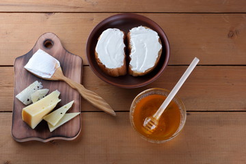 Hard cheese on a wooden board, sandwiches with soft cheese, honey in glass dishes, copy space, minimalism, cheese pattern, wooden background, healthy food, wooden cutlery, simple food