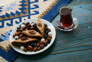 Novruz tray plate with Azerbaijan national pastry pakhlava with sweet snack and glass of traditional black tea on wooden table with green semeni wheat grass background , spring celebration